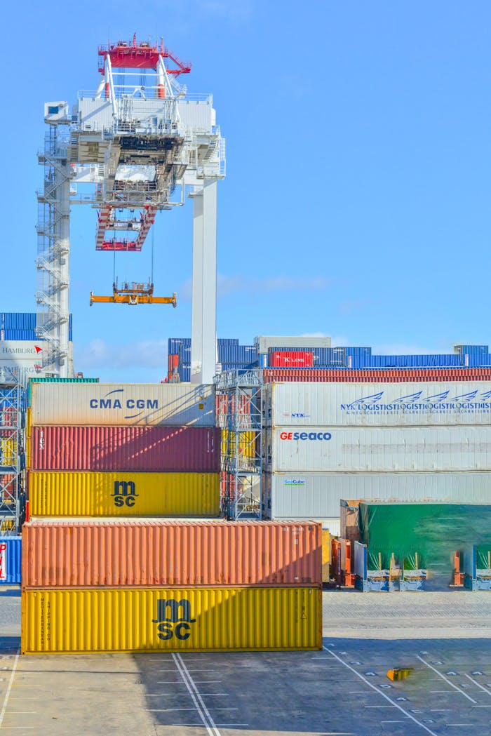 Home Stacked cargo containers in a sunny port industrial setting with crane.